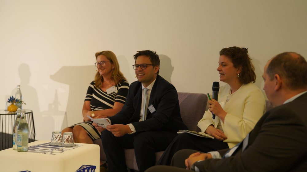 Vier Teilnehmende einer Diskussionsrunde tauschen sich auf der Bühne intensiv aus, während eine Referentin in das Mikrofon spricht.